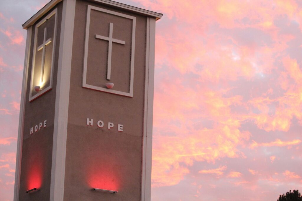 Illuminated church tower with crosses against a vibrant sunset sky.