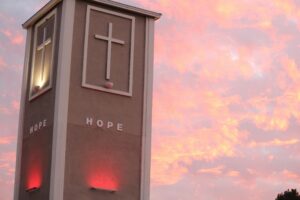 Illuminated church tower with crosses against a vibrant sunset sky.