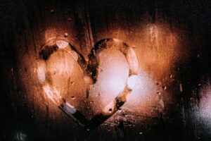 A heart shape drawn on a steamy window with warm, bokeh lighting.