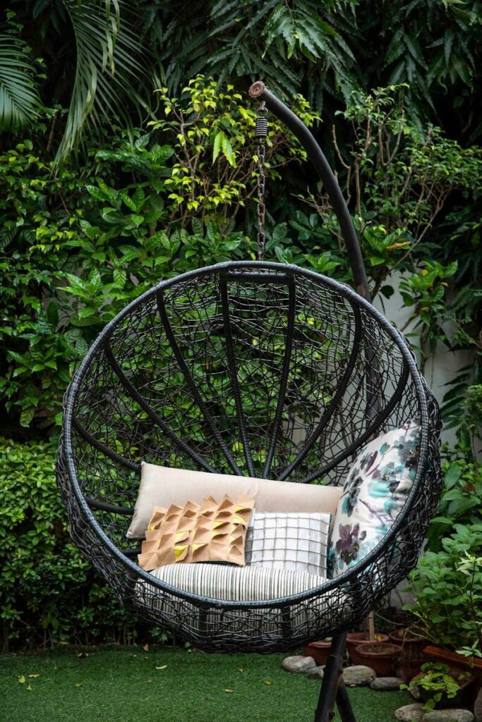 A stylish outdoor swing chair with pillows, set in a vibrant green garden, perfect for relaxation.