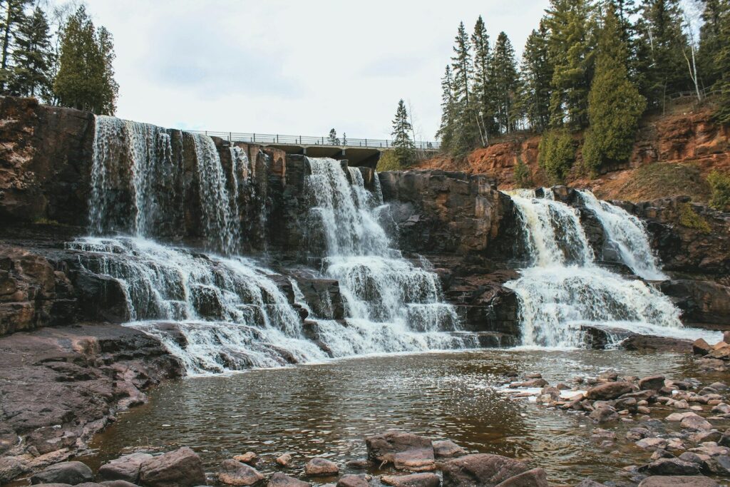 waterfalls near green trees under white sky during daytime